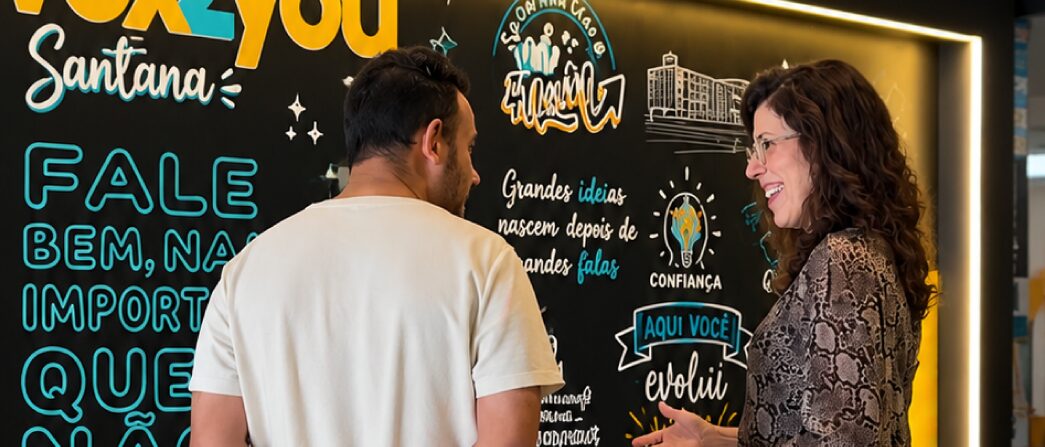 Equipe da Vox Santana apresentando os treinamentos para uma pessoa em frente à parede ilustrada da unidade